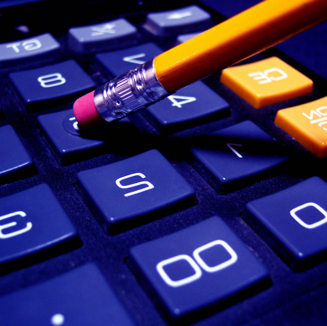 Close up image of a calculator and someone using the eraser end of a pencil to type numbers into the display.